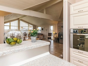 A spacious kitchen with a granite countertop, a refrigerator, and a dining area with wicker furniture. - 5 Star Holiday Home in Lokken (Lokken)