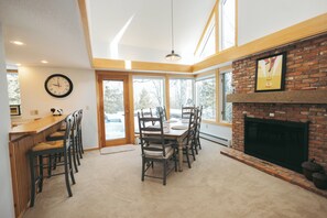A dining area with a brick fireplace, wooden chairs, a round table, and a clock on the wall. - Spacious 4BR 4Bath Home w/Front Door Shuttle to Stratton Mountain (Winhall)