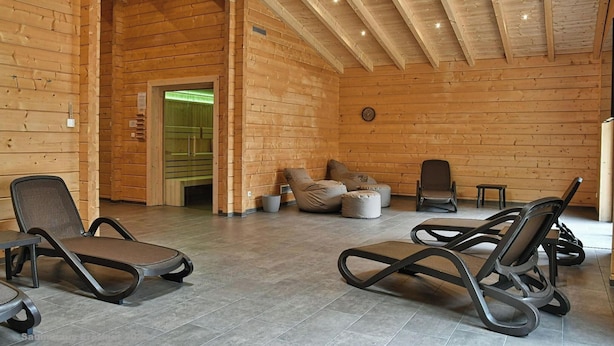 Interior em madeira com poltronas, um sofá e um relógio na parede.