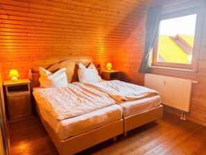 A wooden-paneled bedroom with a bed, two bedside tables, a window, and a radiator. - Doppelhaushaelfte in Hasselfelde (Oberharz am Brocken)