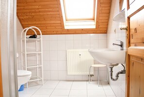 A small bathroom with a skylight, white tiles, a toilet, a white radiator, a sink, and wooden cabinetry. - Doppelhaushaelfte in Hasselfelde (Oberharz am Brocken)