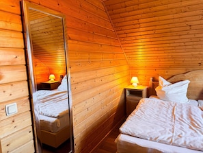 A cabin room with wooden walls, a bed, a nightstand with a lamp, and a mirror. - Doppelhaushaelfte in Hasselfelde (Oberharz am Brocken)