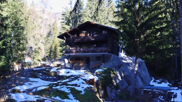 A chalet with a balcony, surrounded by snow and trees.