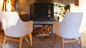 A cozy room with a stone fireplace, two patterned chairs, a wooden floor, and a lamp.