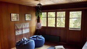 A cozy room with wooden walls and ceiling, a large window, and a seating area with bean bags and a rug.