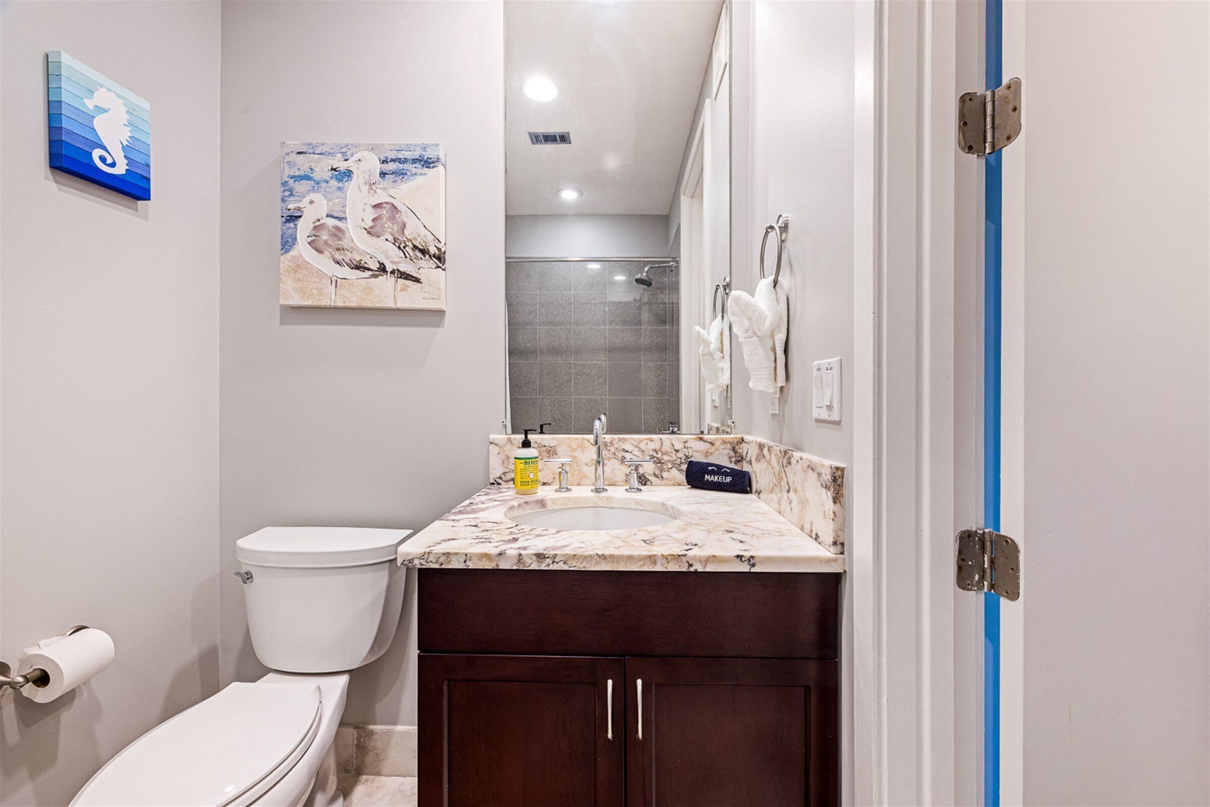 Une salle de bain avec des toilettes, un lavabo et une douche. Des serviettes sont accrochées au mur et un tableau est suspendu au-dessus du lavabo.