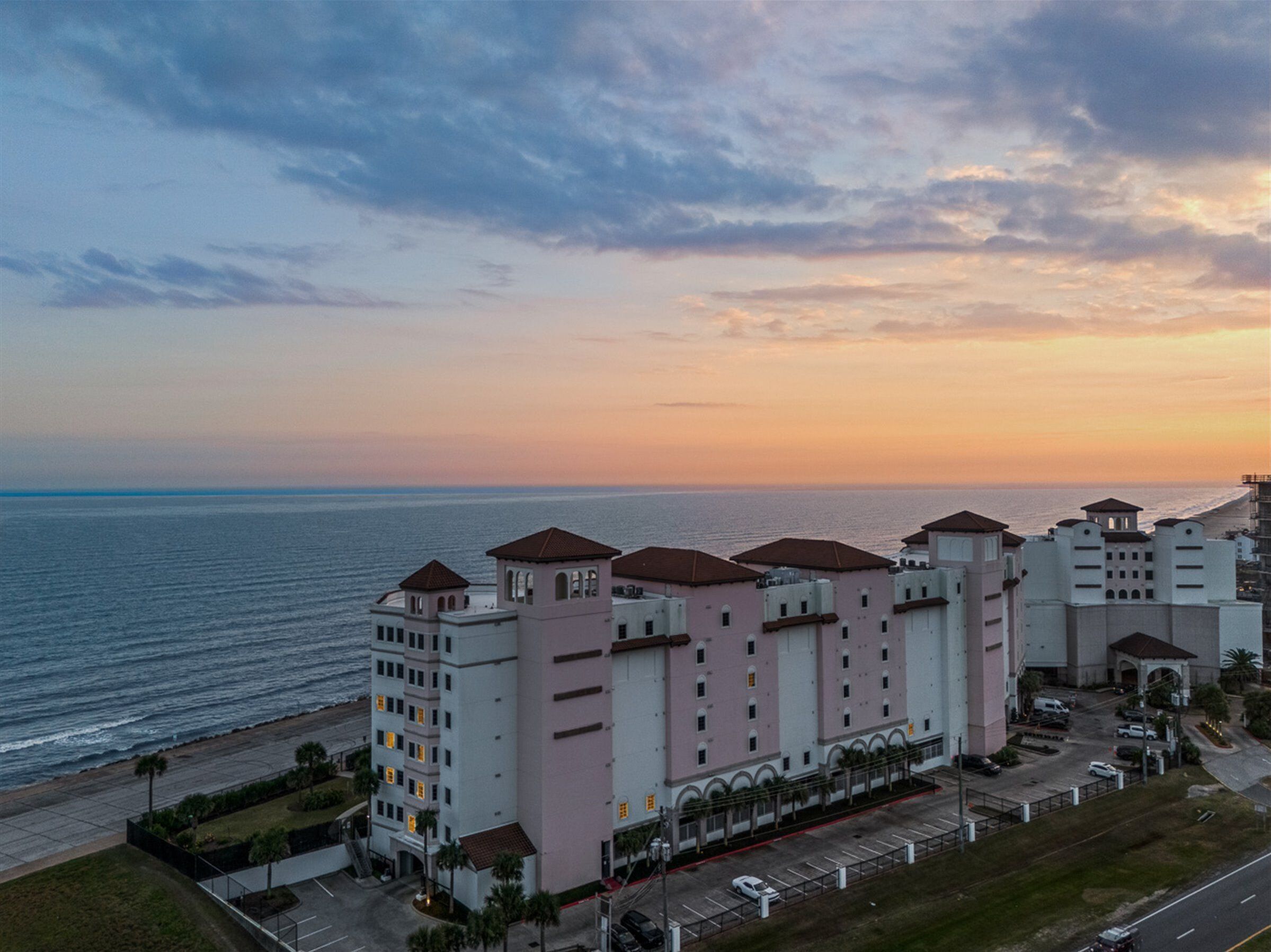 A coastal hotel with multiple buildings, a parking lot, and a view of the sea.