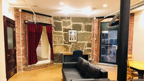 A cozy living area with a stone wall, a black leather sofa, a wooden table, and a red curtain. - Enjoyable 2-bedroom lower level apartment in charming Lynn (Lynn)
