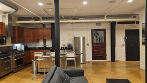 A modern kitchen with stainless steel appliances, a dining area with bar stools, and a living space with a sofa. - Enjoyable 2-bedroom lower level apartment in charming Lynn (Lynn)