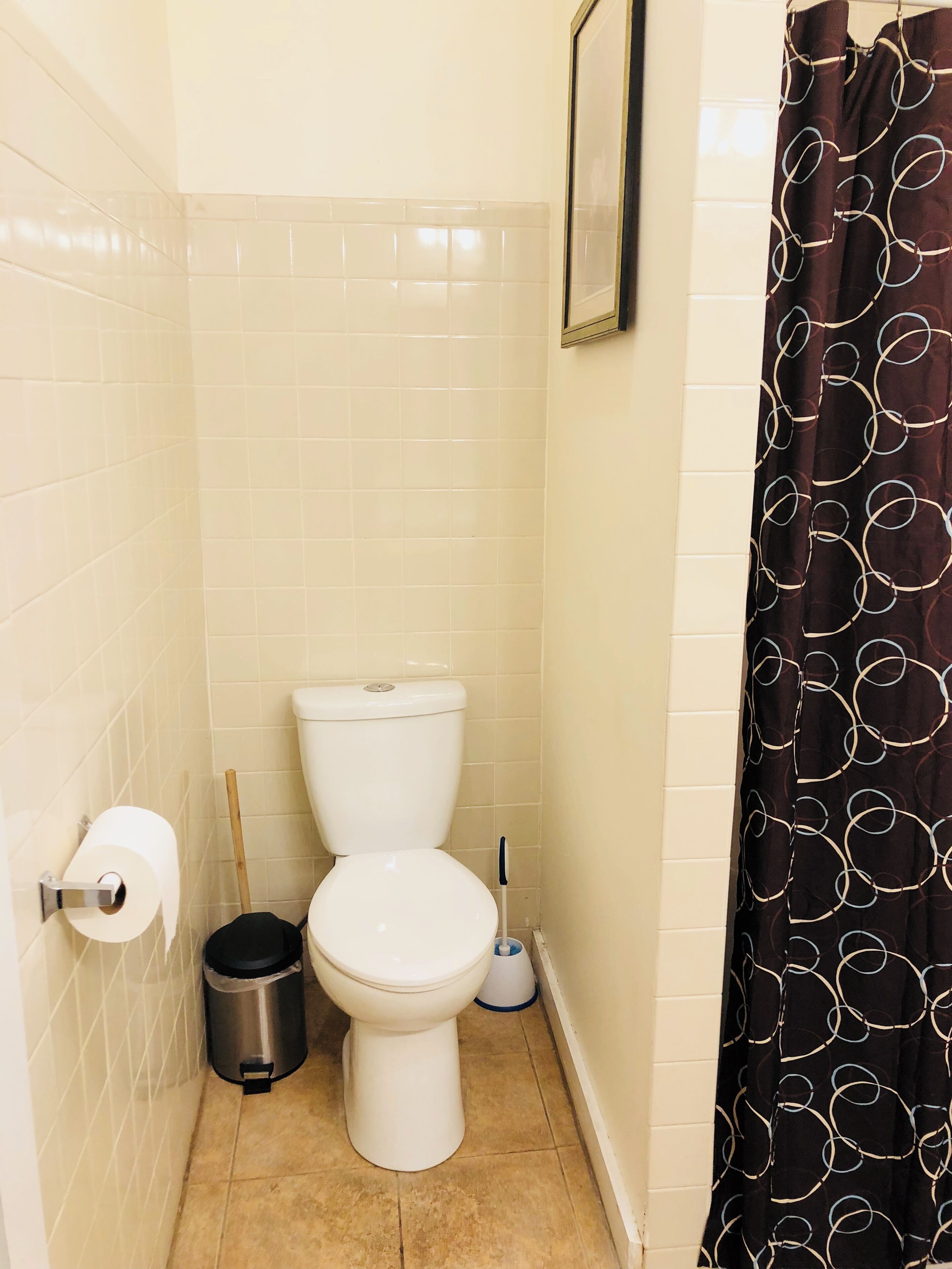 A small bathroom with a toilet, a trash bin, a toilet paper holder, and a shower curtain.