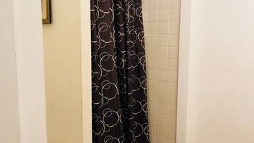 Un baño con cortina de ducha de estampado circular, una puerta blanca con ganchos y un pequeño tapete en el suelo.