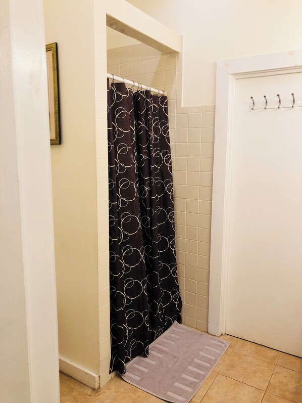 A bathroom with a shower curtain featuring a circular pattern, a white door with hooks, and a small rug on the floor.