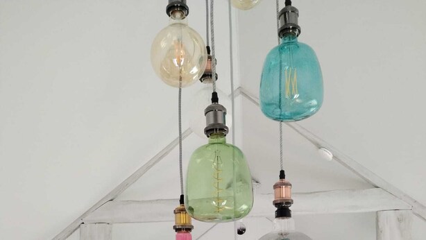 Een kamer met een loft-plafond, zichtbare balken en een hanglamp met meerdere gekleurde glazen lampen.
