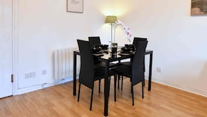 Un coin repas avec une table dressée pour quatre personnes, des chaises noires, un lampadaire et une citation inspirante encadrée accrochée au mur.