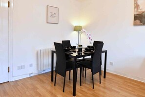 A dining area with a table set for four, black chairs, a floor lamp, and a framed inspirational quote on the wall. - Parking|Sleeps 8| 3 Bedroom House| City Centre (Edinburgh)