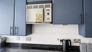Une cuisine avec des meubles de couleur bleue, un réfrigérateur en acier inoxydable, une bouilloire et une machine à café.