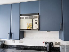 A kitchen with blue cabinets, a stainless steel refrigerator, a kettle, and a coffee maker. - Parking|Sleeps 8| 3 Bedroom House| City Centre (Edinburgh)