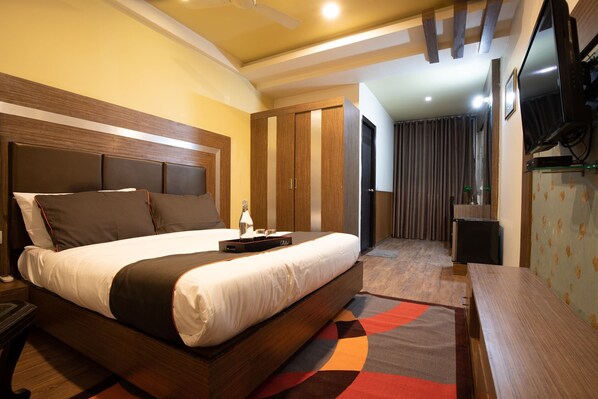 Habitación de hotel con una cama grande, un escritorio, un televisor y un armario.