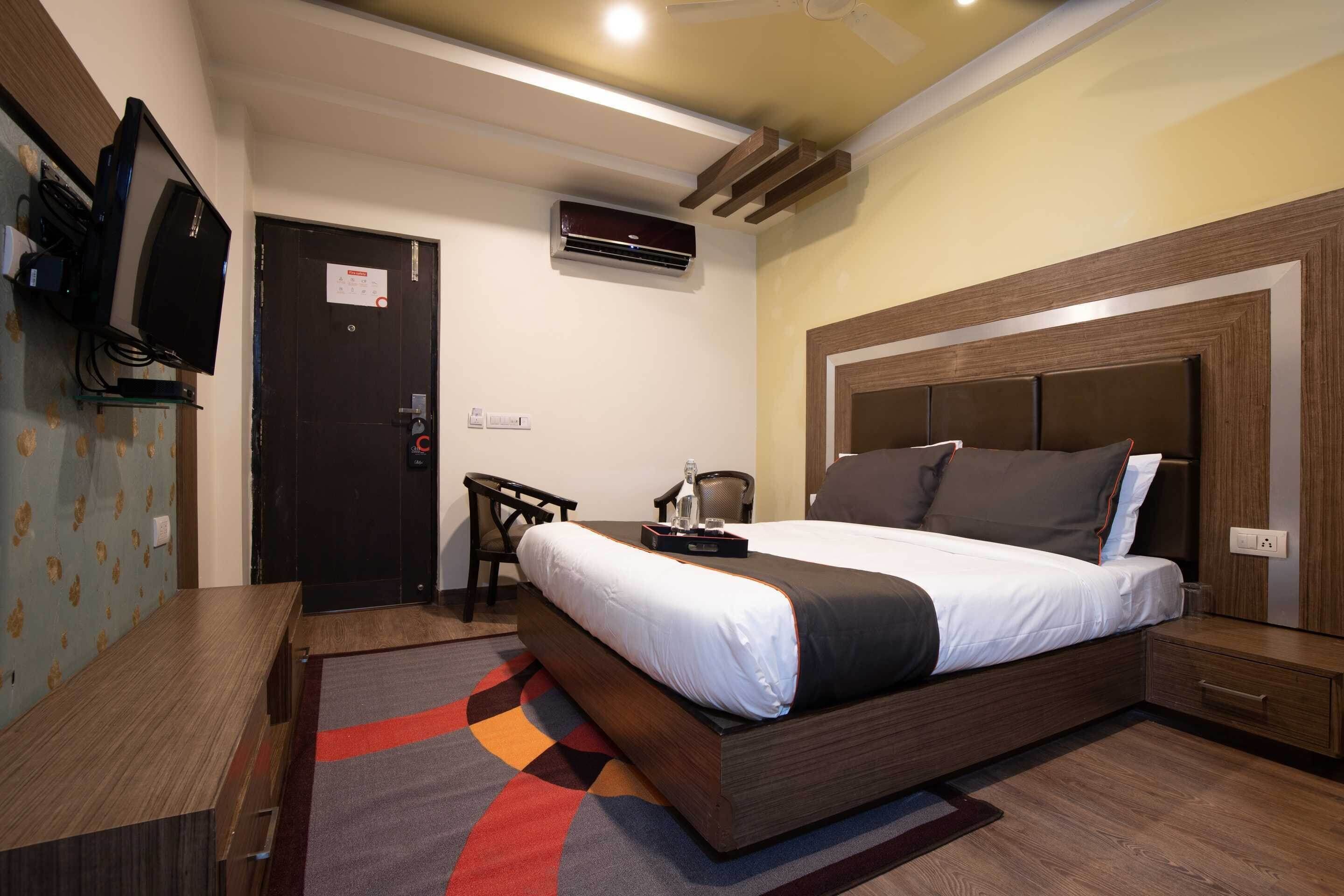 A hotel room with a bed, bedside table, desk, chair, and an air conditioning unit.