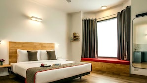 A hotel room with a wooden headboard, a large bed, a bedside table with a lamp, a window with curtains, and a built-in bench under the window. - Collection O Thrissur Zoo & Museum (Thrissur)