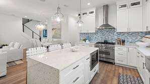 A modern kitchen with white cabinets, a large island, stainless steel appliances, and pendant lighting. - Golf Cart Perks, Large Private Pool, Close to Beach (Santa Rosa Beach)