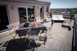 A rooftop terrace with a table and chairs, a potted plant, and a bottle of orange juice. - Appartment with terrasse 40m2 (Sélestat)