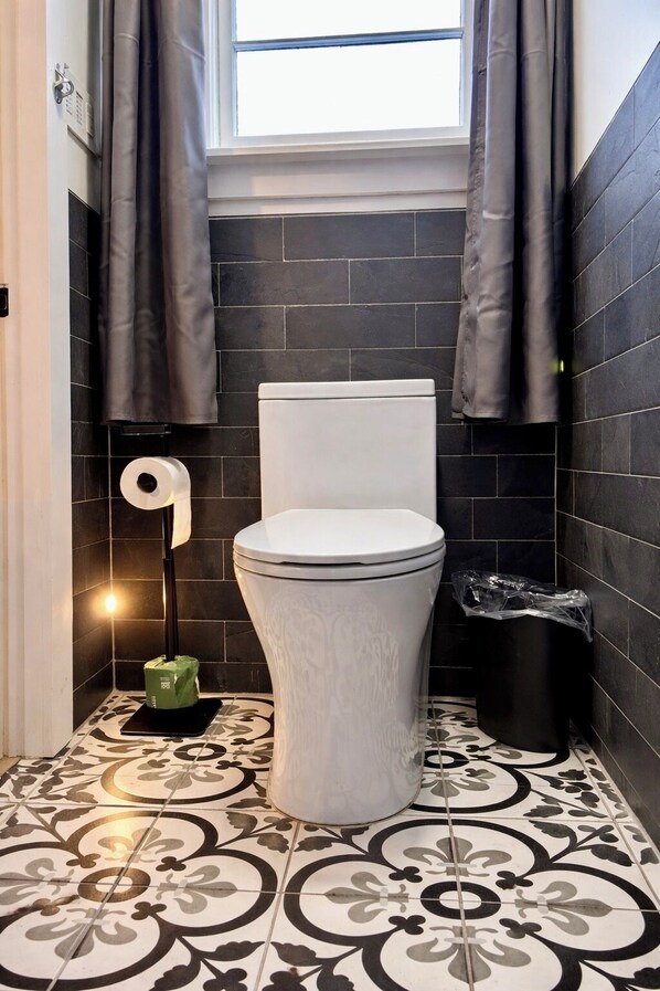 A modern bathroom with a toilet, dark tiled walls, and patterned floor tiles.