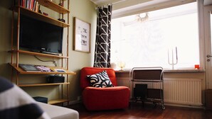 A living room with a red armchair, a bookshelf, a framed picture, a radiator, and a window with a curtain.