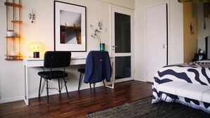A bedroom with a bed, a desk with a chair, a lamp, a framed picture, and a door.