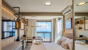 Moderni hotellihuone, jossa on suuri sänky, ruokailutila ja näkymä merelle.