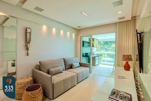 A modern living room with a sofa, wicker baskets, a book, and a TV. - Stay in Ondina with direct beach access (Salvador)