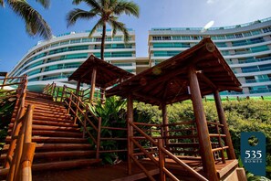 A wooden staircase leading to a covered area with a modern building in the background. - Stay in Ondina with direct beach access (Salvador)