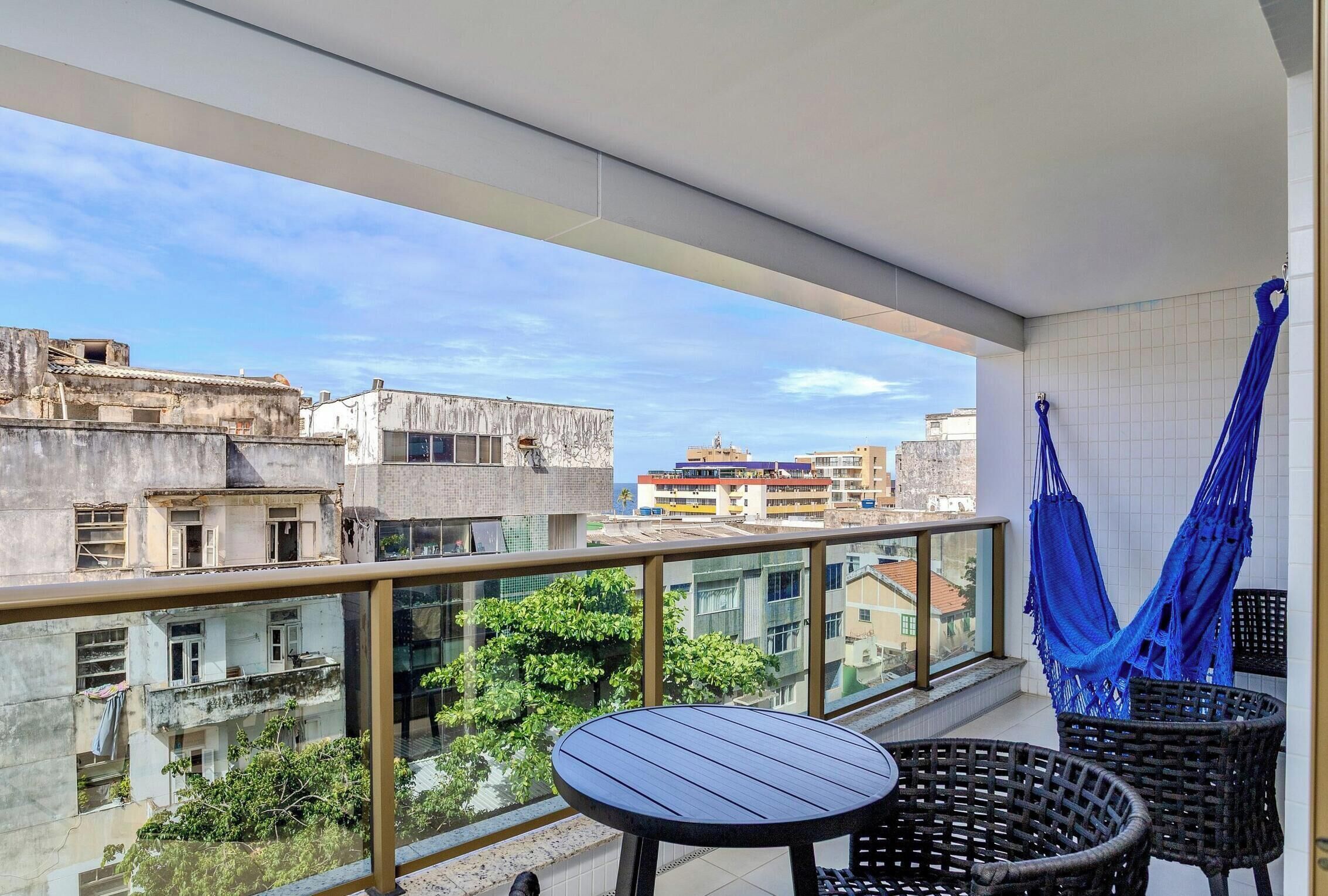 Un balcón con una mesa, sillas, una hamaca y vistas a edificios.