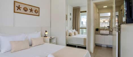 Habitación de hotel con cama, lámpara de noche, espejo, baño con lavamanos y vistas al exterior.