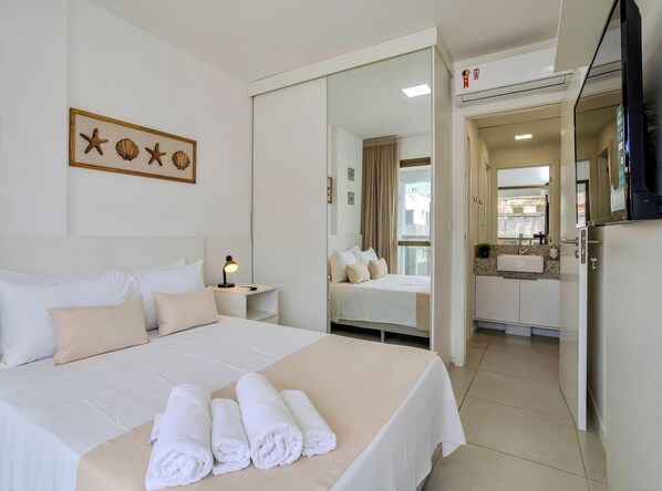 A hotel room with a bed, a bedside lamp, a mirror, a bathroom with a sink, and a view of the outside. - Stay in the heart of Barra, 300m from the beach (Salvador)
