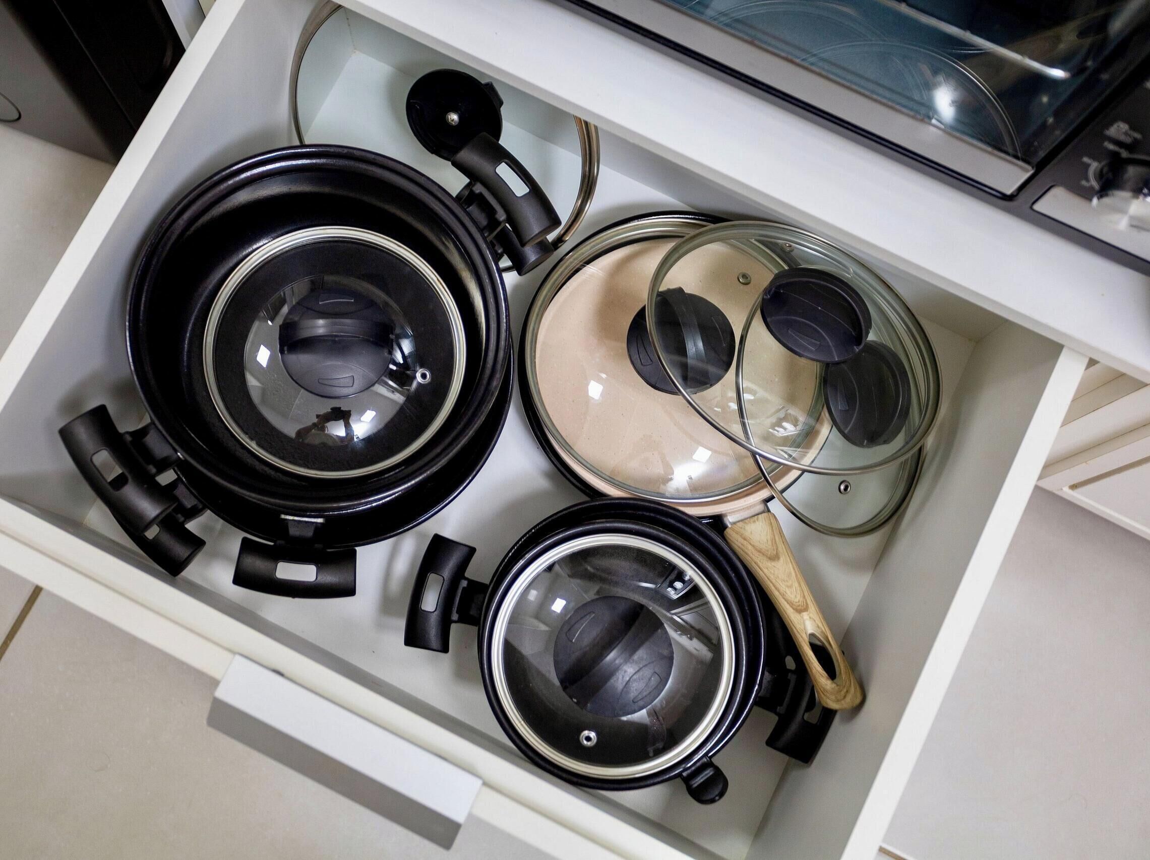 Un cajón de cocina con diferentes utensilios de cocina, como ollas, sartenes y tapas.