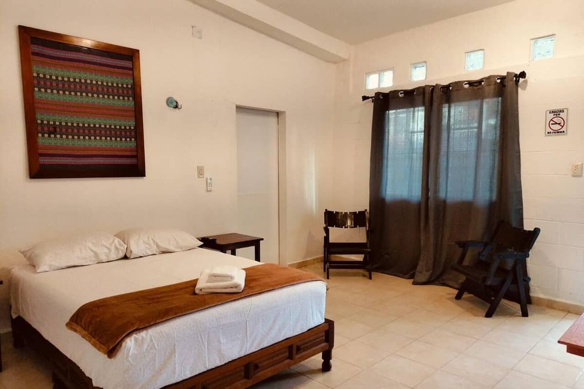 A bedroom with a large bed, a chair, a desk, and a window with curtains.