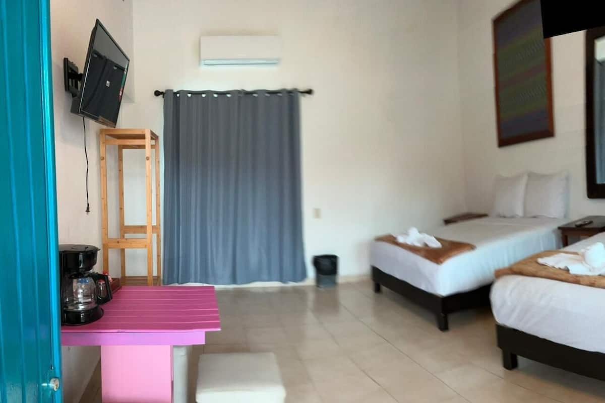 A hotel room with two beds, a desk with a chair, a TV mounted on the wall, and a window with curtains.