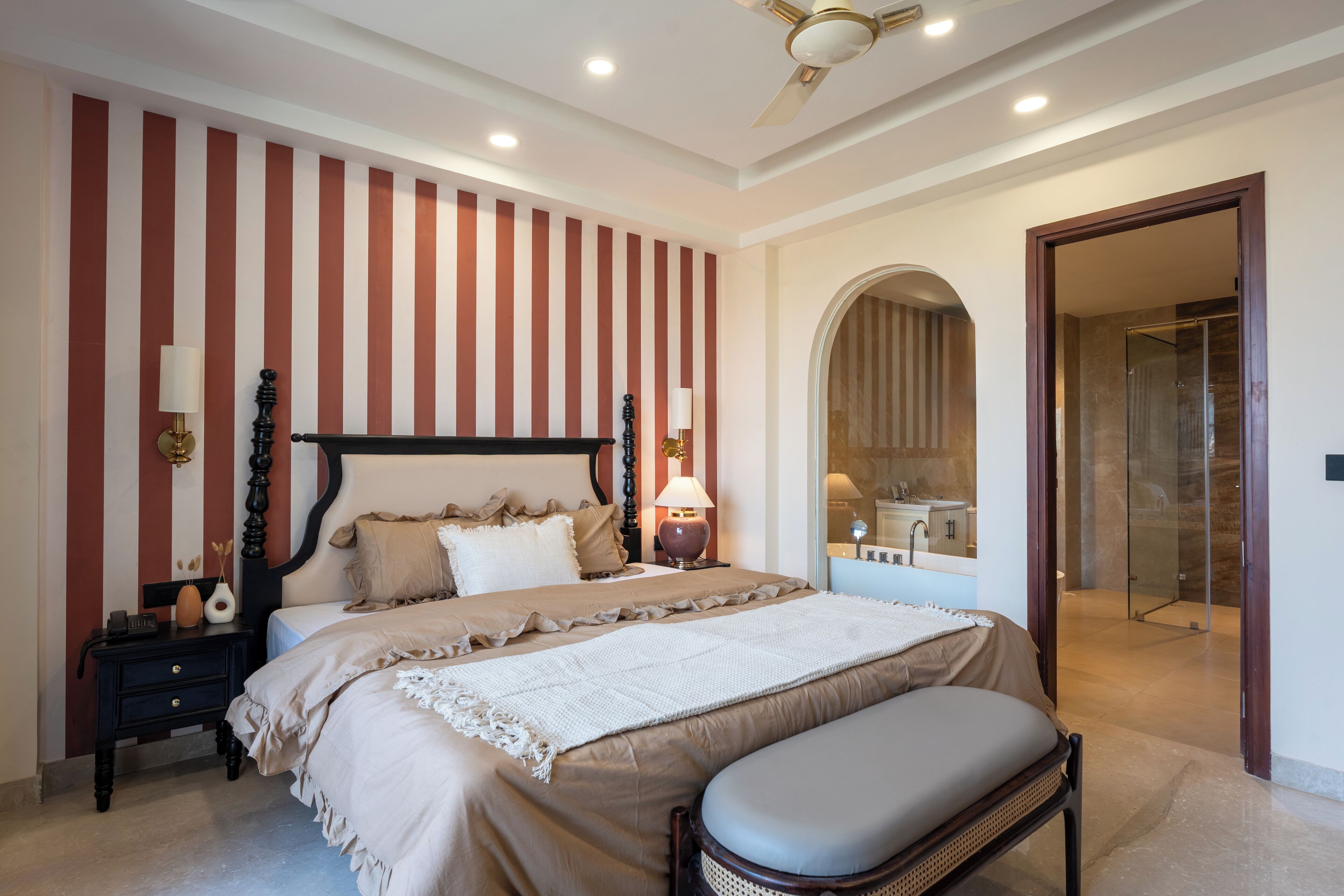 A bedroom with a large bed, a bedside table with a lamp, and a bench.