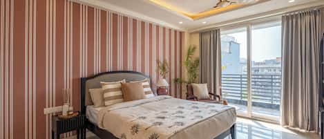 A modern bedroom with a large bed, a nightstand, a lamp, and a view of the city through large windows.