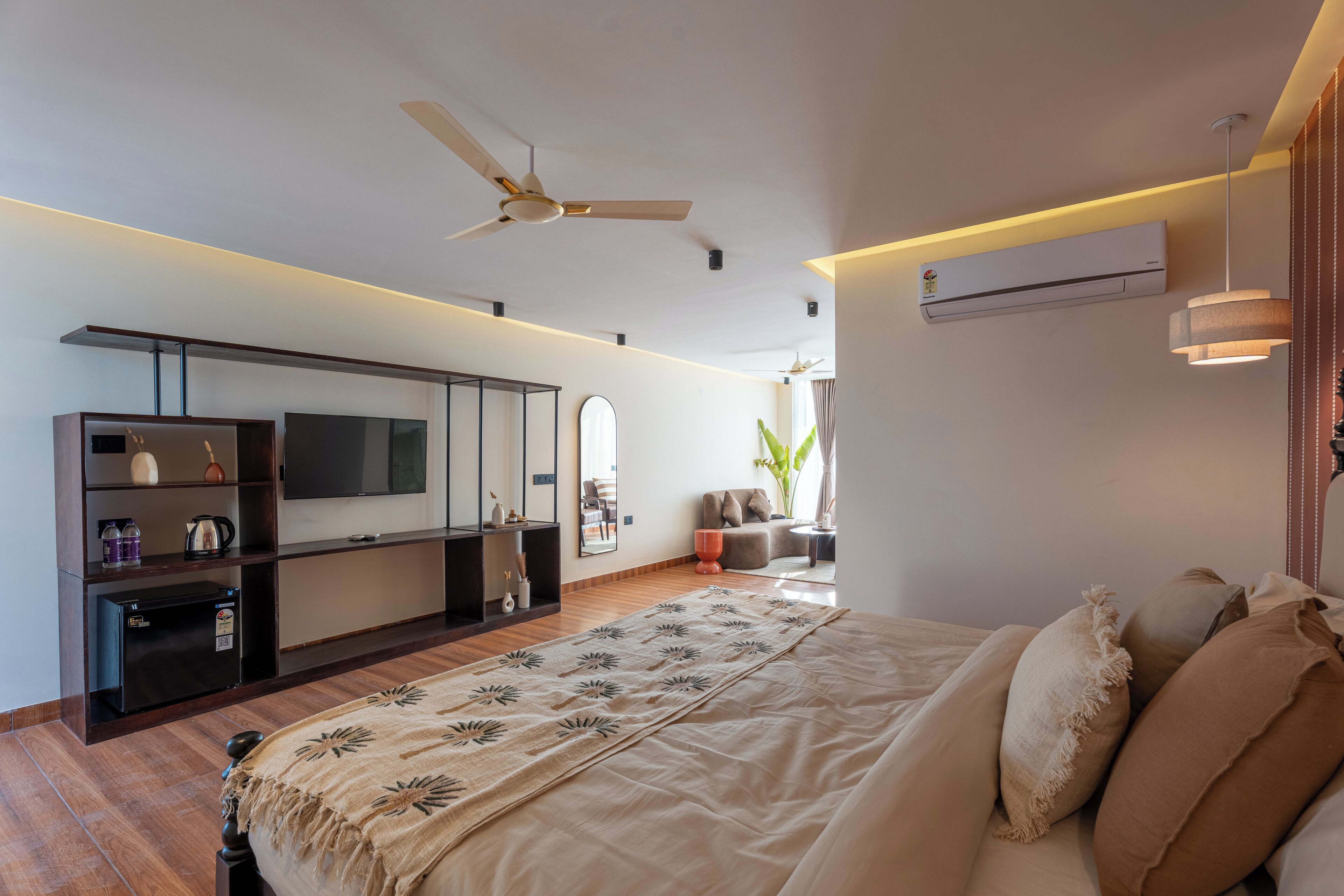 A modern bedroom with a bed, a TV, a ceiling fan, and a small refrigerator.