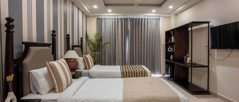 A hotel room with two beds, a ceiling fan, a TV, a bookshelf, and a large window with curtains.