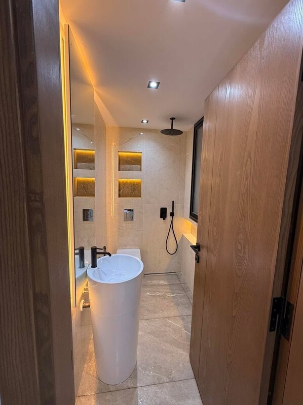 A modern bathroom with a freestanding bathtub, recessed lighting, and a wooden door.