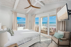 Ein Schlafzimmer mit Bett, Stuhl, Fernseher und Blick auf den Strand.