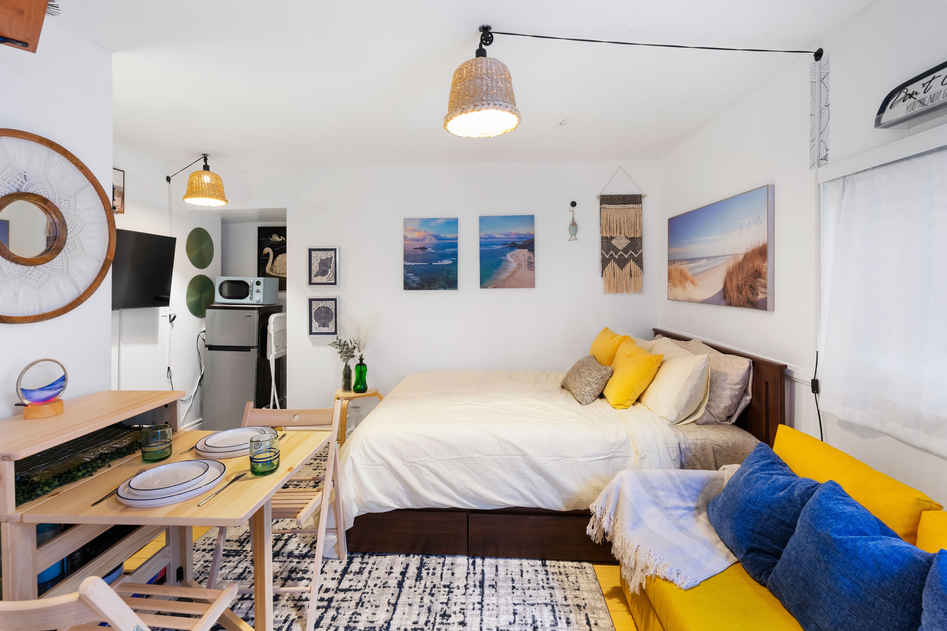 A modern, well-lit bedroom with a bed, bedside table, and a dining area with a table and chairs.