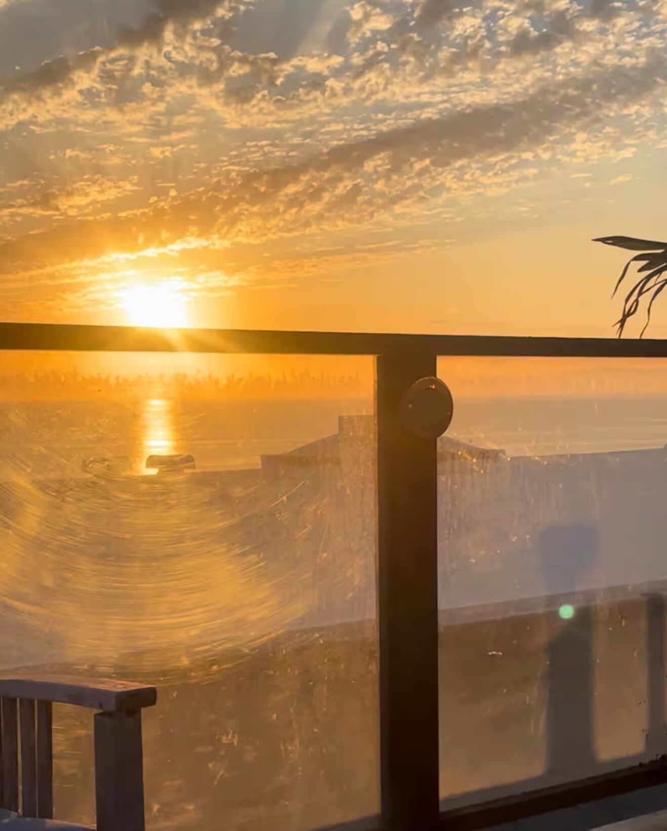 A sunset view from a balcony with a railing, overlooking a cityscape and a body of water.