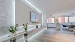 Un intérieur moderne avec un long comptoir d’accueil, des plantes en pot, une œuvre d’art encadrée et une vue sur la cuisine et l’espace repas.