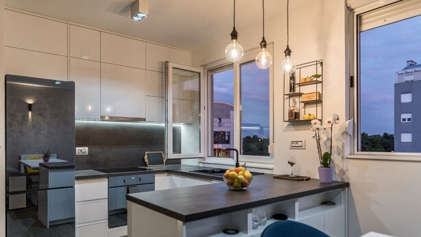 Une cuisine moderne dotée d’un îlot central, d’appareils électroménagers intégrés et de luminaires suspendus.