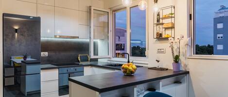 A modern kitchen with a central island, a built-in oven, and a window overlooking a cityscape.