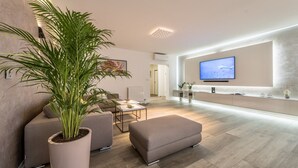 Un salon moderne doté d’un téléviseur à écran plat, d’une grande plante en pot et d’un aménagement minimaliste.